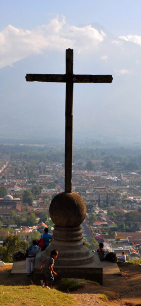 An ancient stone cross overlooking Guatemala city with volcanoes in the background