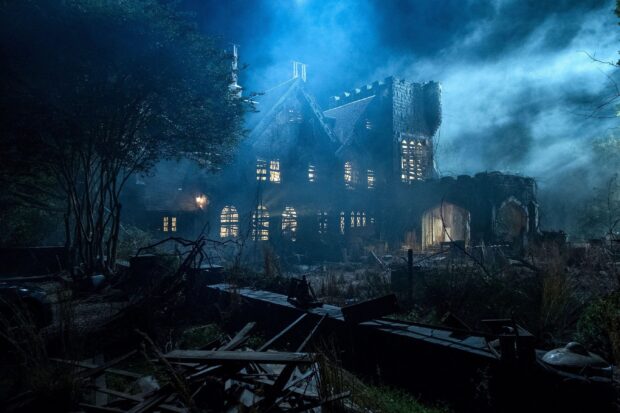A haunted house surrounded by trees and fog at night with glowing windows and eerie atmosphere