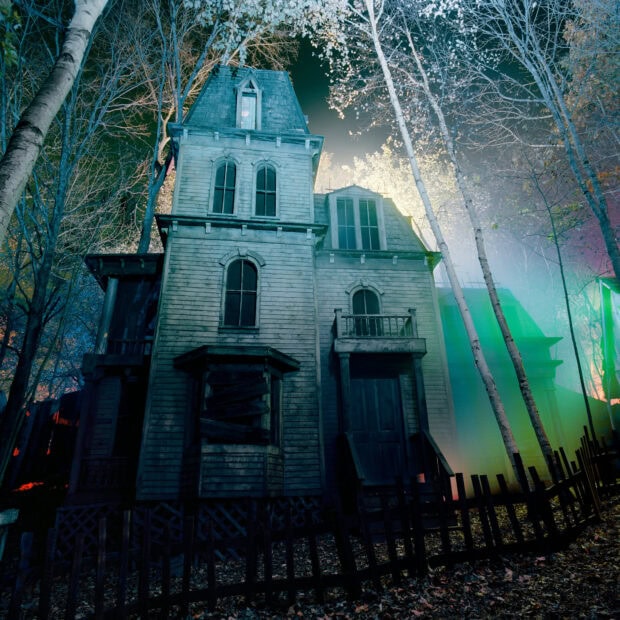 Old abandoned haunted house surrounded by bare trees in eerie forest at night