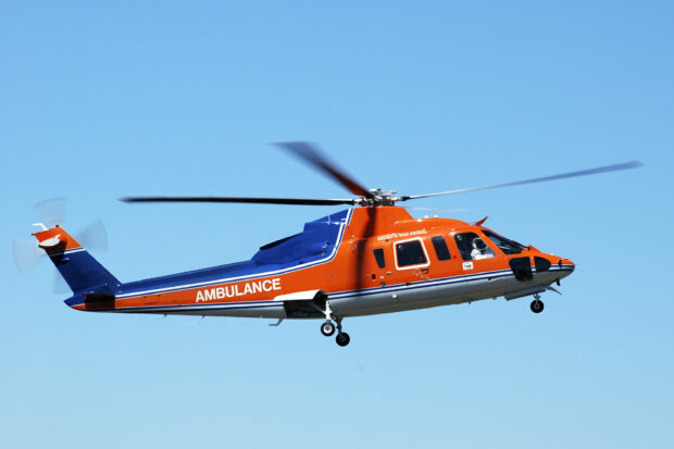 A helicopter ambulance flying in clear blue sky with orange and blue colors