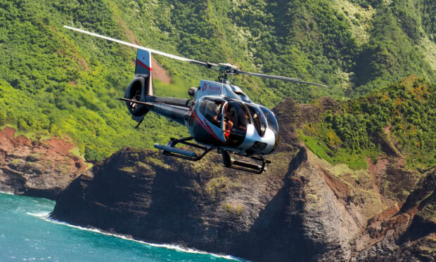 A helicopter flying over a coastal landscape with green cliffs and blue ocean water