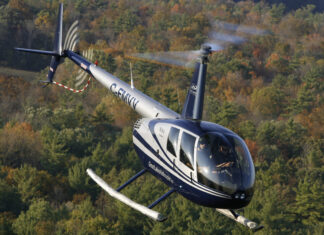 A blue helicopter flying over a forest with autumn trees in the background