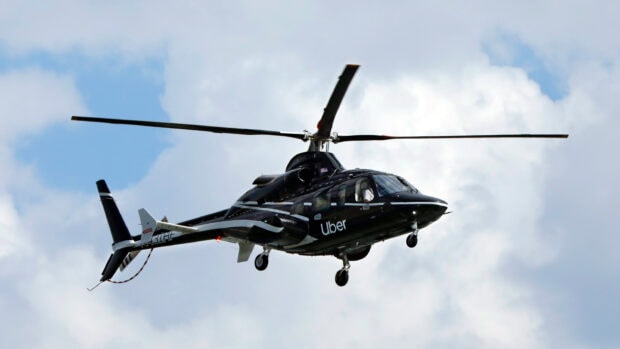 Black helicopter with Uber logo flying in cloudy sky with clear details