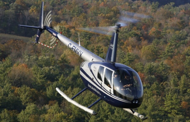 A blue helicopter flying over a forest with autumn trees in the background