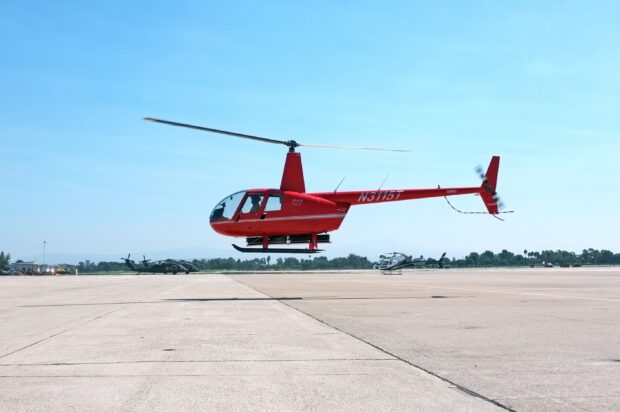 Red helicopter hovering above the airport runway on a clear sky day
