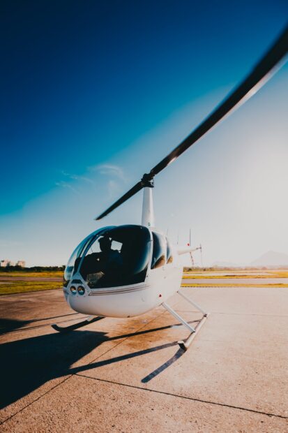 A white helicopter with a pilot inside parked on a runway under a clear blue sky