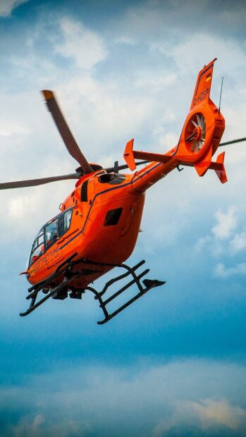 Bright orange helicopter flying in cloudy sky with rescue markings