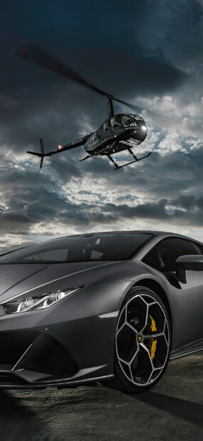 A helicopter flying above a sleek sports car under a cloudy sky at dusk