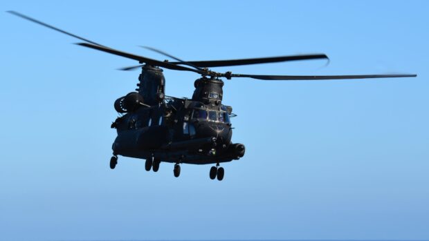 Black military helicopter flying in the clear blue sky with visible rotor blades