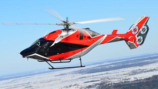 Red and black helicopter flying over snowy landscape with clear blue sky