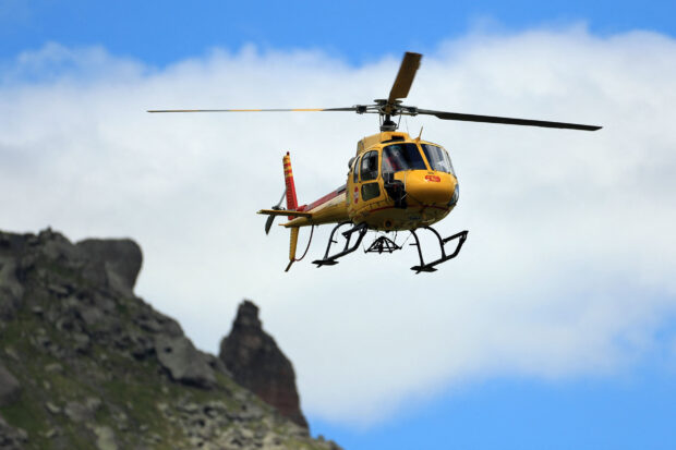 Yellow helicopter flying over rocky mountain landscape in clear sky
