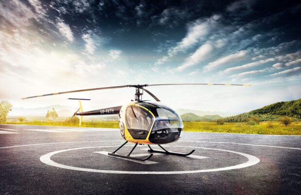 A yellow and black helicopter on a landing pad in a scenic outdoor environment with hills and clouds