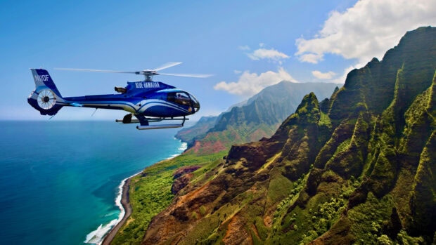 Blue Hawaiian helicopter flying over lush coastal cliffs and ocean