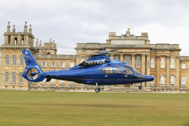 Blue helicopter flying over a historic mansion on a green lawn