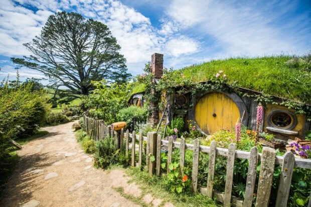 A charming Hobbiton house with a yellow door surrounded by lush greenery and a wooden fence