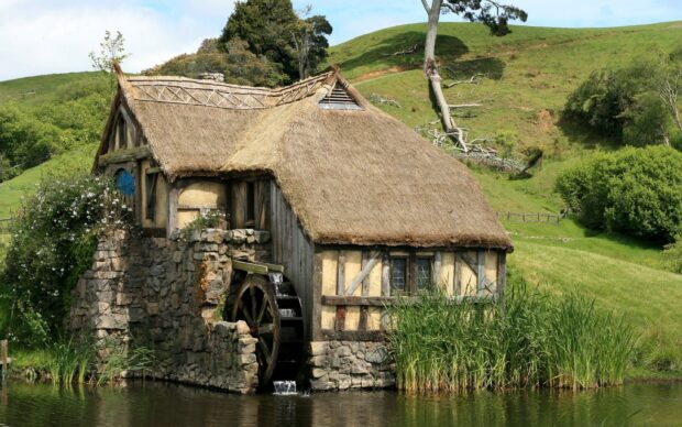 A rustic watermill house in Hobbiton surrounded by green hills and a peaceful pond