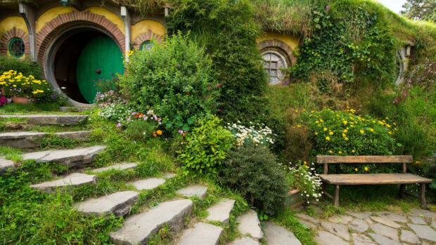 A charming hobbit house with a round green door surrounded by lush greenery and colorful flowers