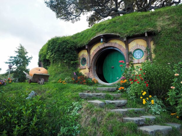A charming hobbit hole with a round green door surrounded by lush greenery and colorful flowers