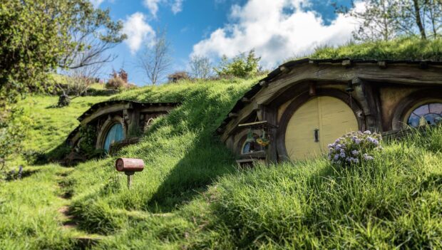 A peaceful view of hobbiton with grass covered homes and a wooden mailbox on a sunny day