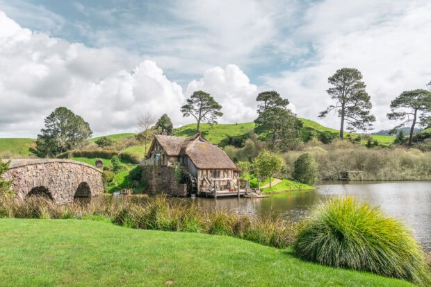 A peaceful watermill house in Hobbiton surrounded by greenery and a stone bridge