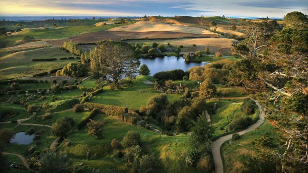 A scenic view of Hobbiton featuring lush green hills and peaceful water bodies in a natural landscape