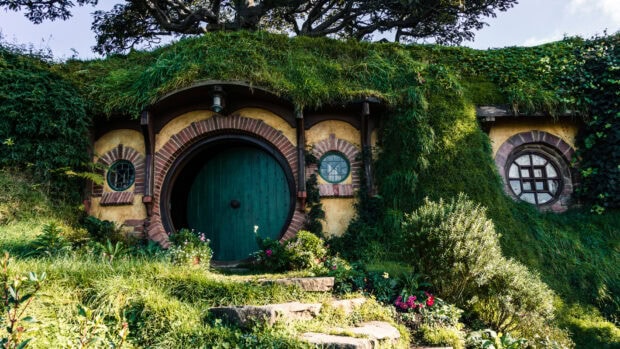 A cozy hobbit house covered in lush greenery with a round door and garden in Hobbiton