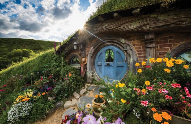 A charming hobbit hole with a blue door surrounded by vibrant flowers and lush greenery