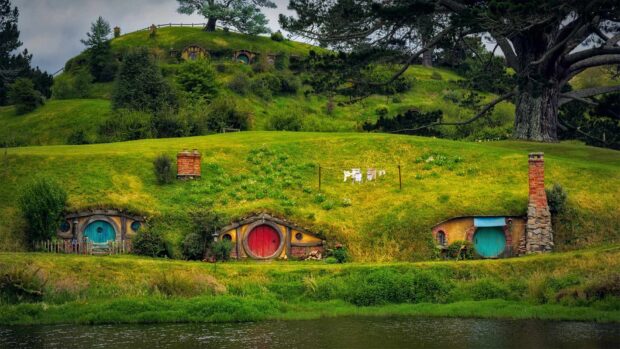 A peaceful hobbit village with round doors nestled in green hills near a calm river