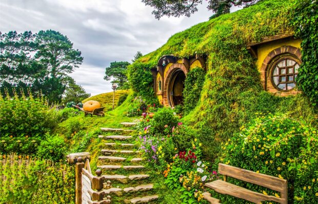 A scenic view of a Hobbiton house surrounded by lush greenery and colorful flowers