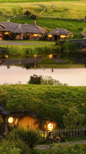 A cozy hobbit hole with round windows and lush greenery in the Hobbiton village