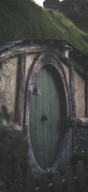 Rustic green wooden door of Hobbiton house with grass roof and bell hanging