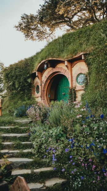 A charming Hobbiton house with a green door surrounded by colorful flowers and lush greenery