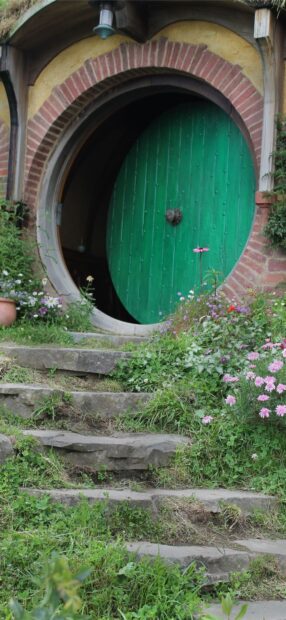 The charming hobbit hole door surrounded by flowers and stone steps in Hobbiton