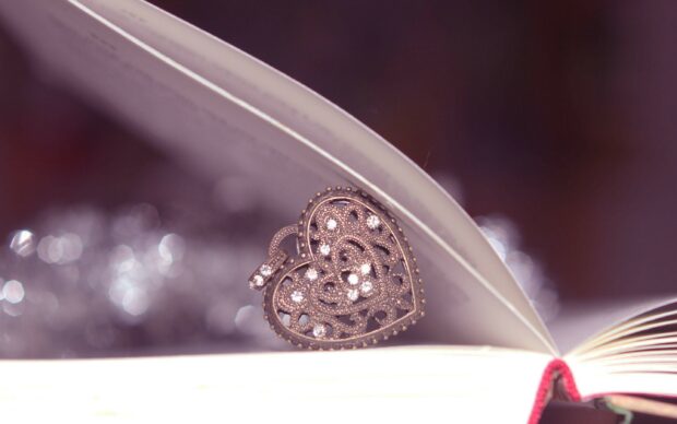 A heart shaped jewel with intricate patterns and sparkling stones placed between the pages of an open book