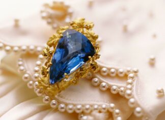 A blue jewel surrounded by golden leaves on a pearl decorated fabric background