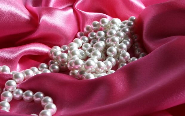 A string of pearls jewels resting on vibrant pink satin fabric