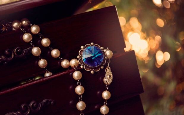 A string of pearls with a blue jewel on a wooden box in warm sunlight background