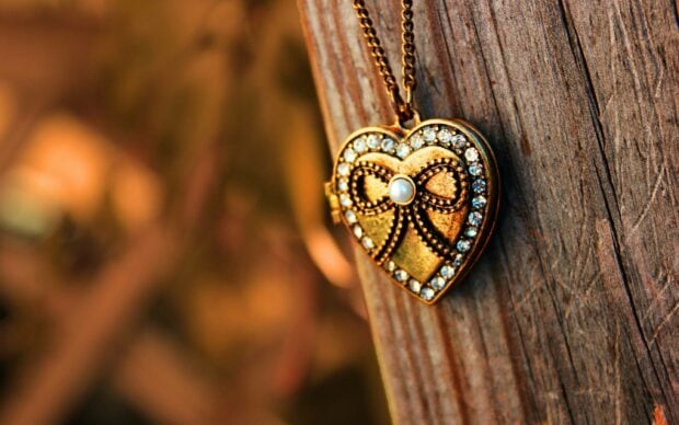 A heart shaped jewel with intricate design and pearls hanging on a wooden surface