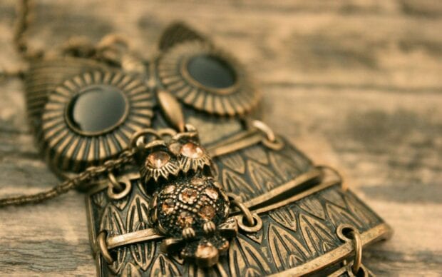 Close up of an antique owl jewels pendant with intricate patterns on wooden surface