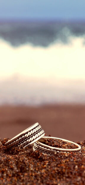 Two silver jewels with intricate patterns resting on sandy surface near the sea shore