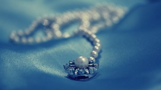 A close up of a jewel featuring a pearl on a blue fabric background
