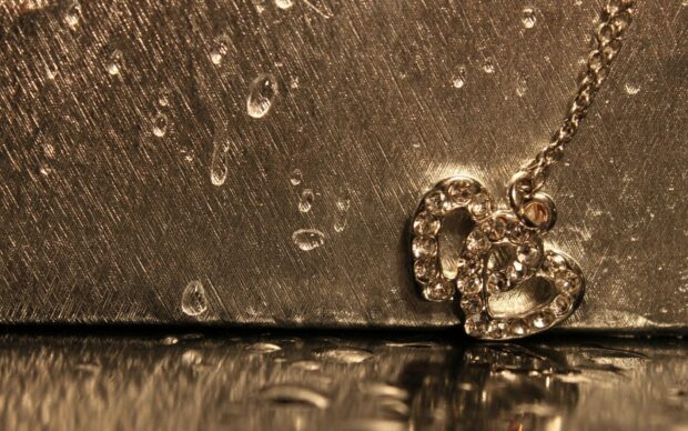 Sparkling jewels heart necklace on a textured surface with water droplets