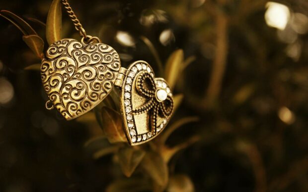 A heart shaped jewel with intricate designs and sparkling stones hanging on a plant branch