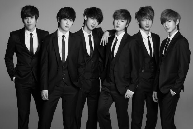 A K Pop group wearing black suits and ties posing together in a studio setting