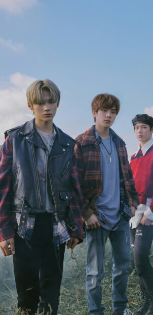 Three young men standing outdoors wearing plaid patterned clothing on a cloudy day