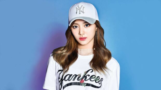 Young woman in a Yankees cap and white shirt posing for K Pop portrait against blue background
