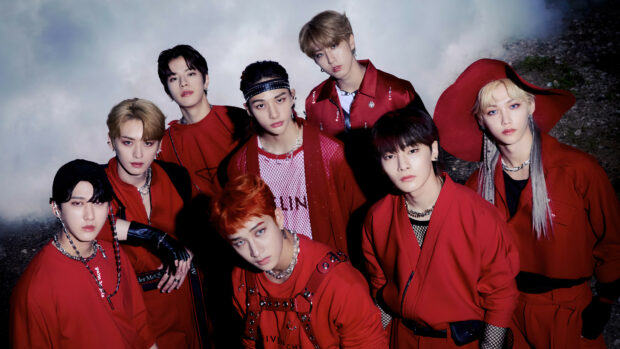 A K Pop group posing together in red outfits with intense looks at night