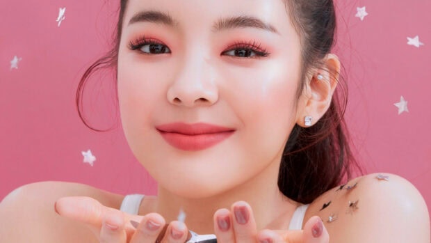 Young woman with star confetti on shoulder and makeup on pink background