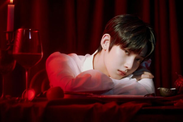 A K Pop artist resting his head on the table in a moody red setting