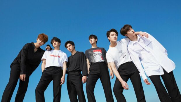 K pop group posing together outdoors under clear blue sky